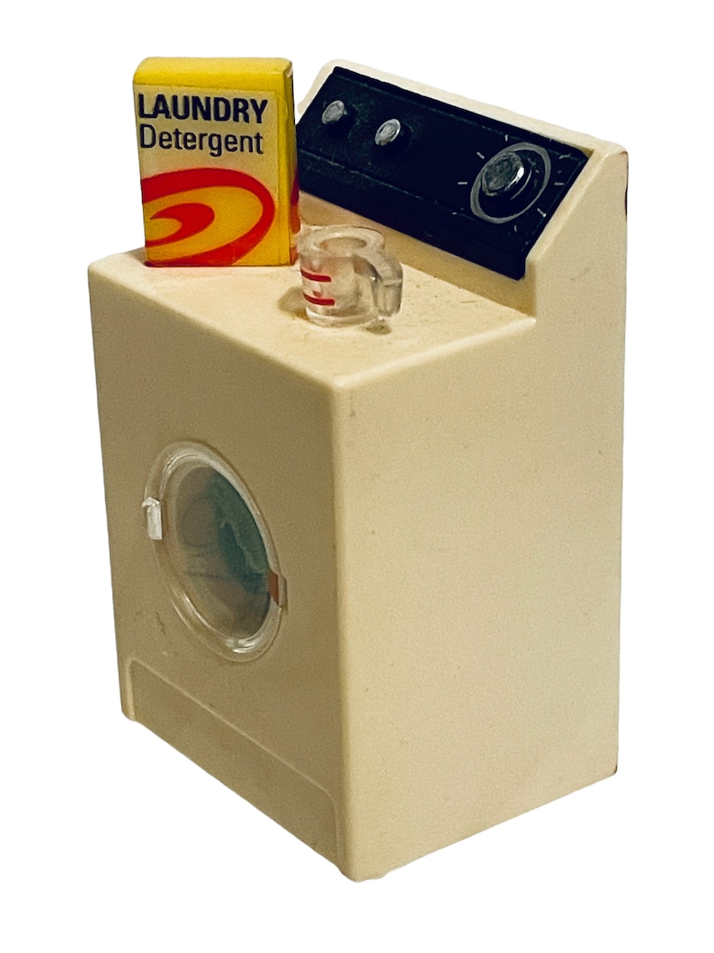 Peut inclure: Une machine &agrave; laver jouet miniature de couleur cr&egrave;me avec une porte transparente. Une bo&icirc;te jaune de "LAUNDRY Detergent" est pos&eacute;e sur le dessus, ainsi qu'un petit verre doseur. Le panneau de commande est noir avec un cadran et deux boutons. Un jouet amusant de style vintage.