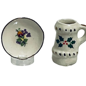 May include: A white ceramic saucer with a floral design and a white ceramic mug with a holly design.
