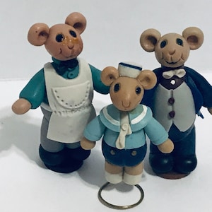May include: Three handmade clay figurines of mice. The mouse on the left is wearing a blue and white apron. The mouse in the middle is wearing a blue sailor outfit with a white hat. The mouse on the right is wearing a black suit with a white bow tie.