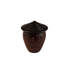 May include: A dark brown wooden urn with a conical lid. The urn has a rounded body with visible wood grain. The lid is a darker shade and has concentric circular ridges. The urn is set against a white background.