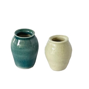 May include: Two small ceramic vases, one teal green and one light beige.