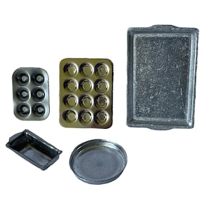 May include: A collection of small, metallic baking pans in various shapes. Includes a rectangular baking sheet, a loaf pan, a round pan, and two muffin tins. The pans are silver and appear to be made of metal.