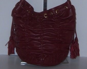 May include: A burgundy leather handbag with a drawstring closure and tassel accents. The bag has a woven design and gold-toned hardware.