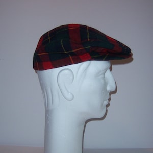 May include: A plaid flat cap in red, green, and yellow. The cap is displayed on a white mannequin head. The cap's pattern is a classic tartan design, with a brim that extends over the forehead.