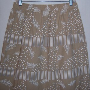 May include: A beige skirt with a white pattern of feathers and dots. The skirt has a wide waistband and a flowing silhouette.