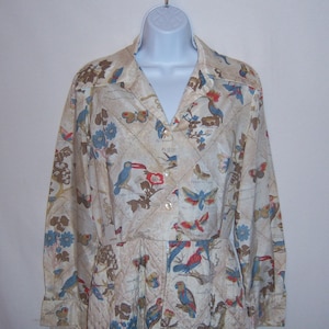 May include: A long-sleeved button-up shirt with a cream background and a pattern of birds and butterflies. The shirt has a quilted texture and a pointed collar.
