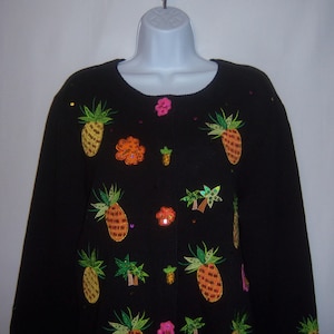 Könnte beinhalten: Schwarzer Strickcardigan mit gestickten Ananas, Palmen und Blumen. Die Stickerei ist mit Pailletten und Perlen ausgeführt.