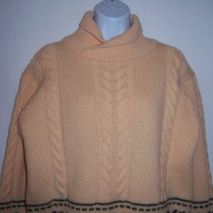 May include: A pale yellow cable knit sweater with a folded collar and a black and white striped band at the bottom.