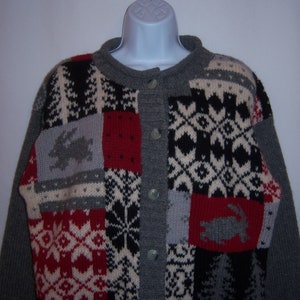 May include: A gray, red, black, and white knitted cardigan with a patchwork design featuring various geometric patterns and animal motifs. The cardigan has a button closure.