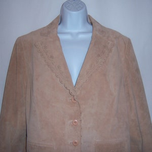 May include: A tan suede jacket with a scalloped lace trim around the collar. The jacket has a button closure and two pockets.
