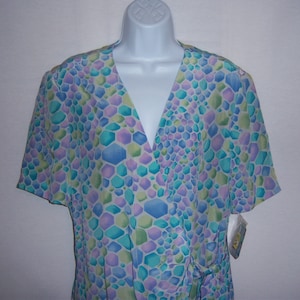 May include: A short-sleeved wrap top in a pastel geometric pattern of blue, green, and purple. The top has a V-neck and a tie closure at the waist. The fabric appears to be lightweight and suitable for warm weather.