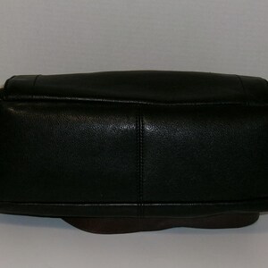 K&ouml;nnte beinhalten: Eine schwarze Lederhandtasche mit abgerundetem Boden und rechteckiger Oberseite. Die Tasche hat eine strukturierte Oberfl&auml;che und eine sichtbare Naht in der Mitte. Der Boden der Tasche ist dunkelbraun.