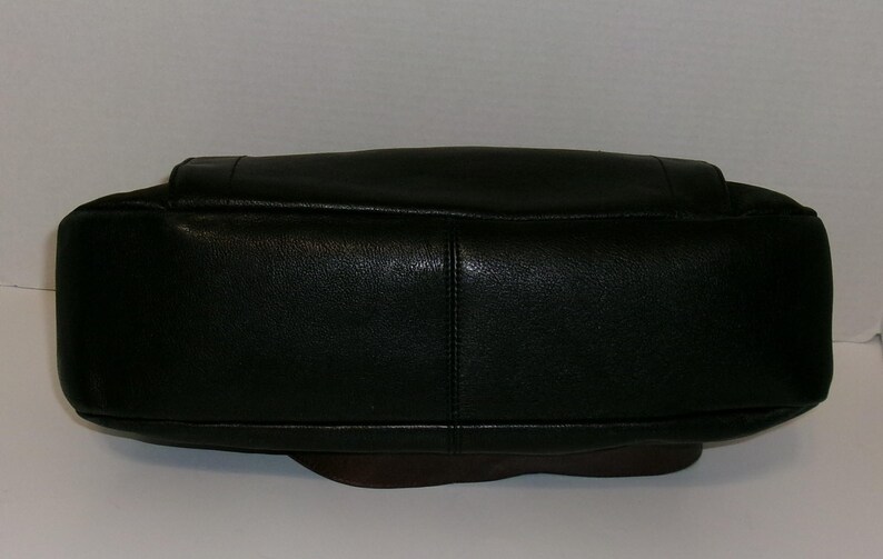 K&ouml;nnte beinhalten: Eine schwarze Lederhandtasche mit abgerundetem Boden und rechteckiger Oberseite. Die Tasche hat eine strukturierte Oberfl&auml;che und eine sichtbare Naht in der Mitte. Der Boden der Tasche ist dunkelbraun.