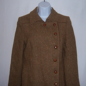 May include: A brown tweed jacket with a double-breasted closure and brown buttons. The jacket has a collar and long sleeves.