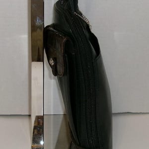 May include: Black leather handbag with a brown crocodile-textured accent pocket and trim. The bag has a long black strap and a silver zipper. The bag is displayed on a silver stand.