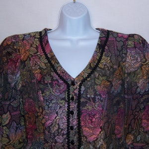 May include: A black and multi-colored floral patterned blouse with a v-neck and button closure. The blouse has black trim around the neckline and down the front.