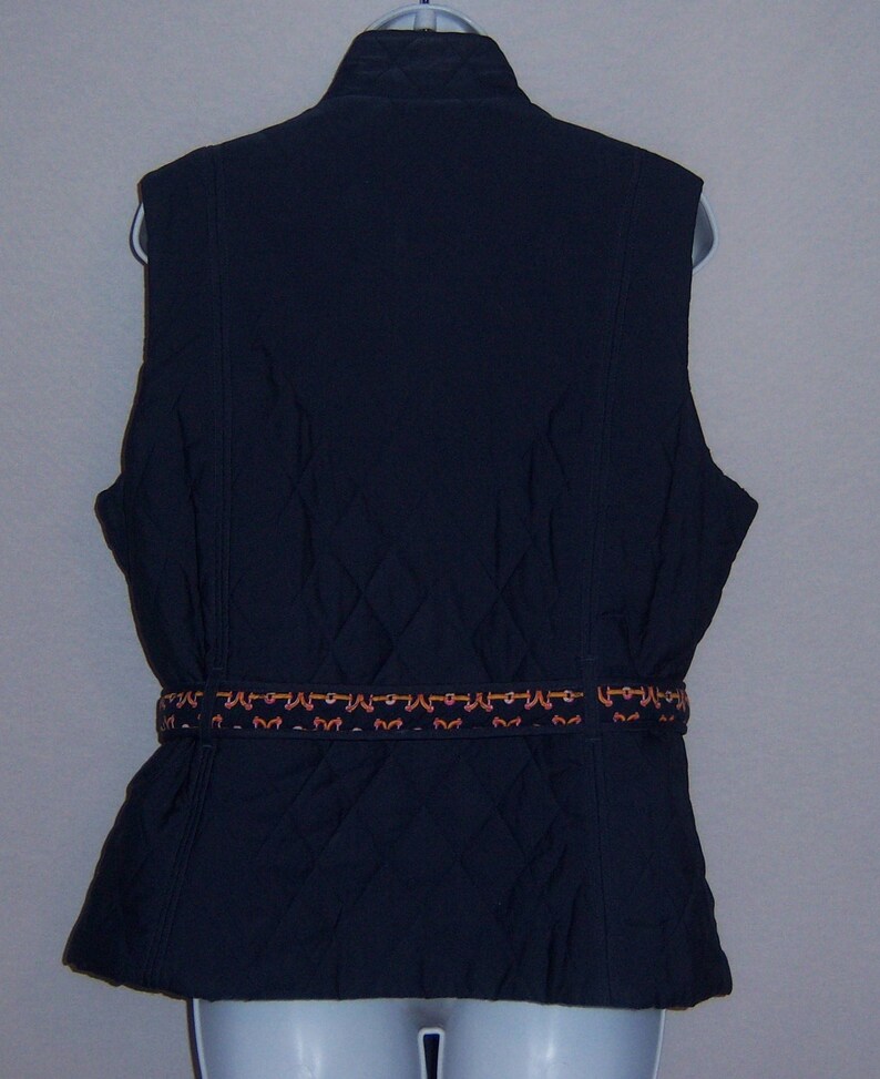 May include: A navy blue quilted vest with a decorative brown and orange belt. The vest has a stand-up collar and a zipper closure.