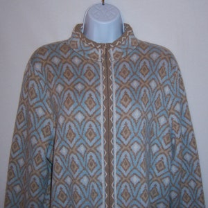 May include: A zip-up jacket with a geometric pattern in shades of blue, tan, and white. The jacket has a high collar and a full-length zipper. The pattern is a repeating diamond design.