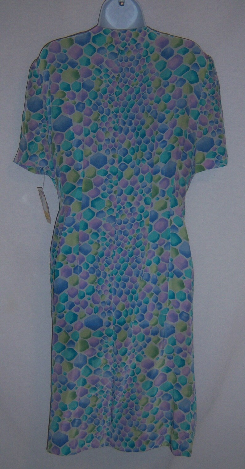 May include: A short-sleeved dress with a geometric pattern in shades of blue, green, and purple. The dress is displayed on a white hanger. The pattern is made up of small, irregular hexagons. The dress has a tag attached.