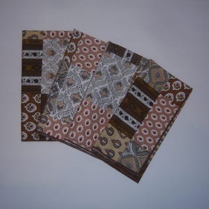 Op de afbeelding: Een verzameling van vier rechthoekige stoffen placemats. Elke placemat heeft een patchwork-ontwerp met verschillende patronen, waaronder bloemen, paisley en geometrische vormen. Het kleurenpalet omvat tinten bruin, beige en wit.