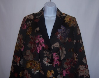 May include: A black blazer with a floral pattern in shades of pink, gold, and brown. The blazer has a black satin collar and a single button closure.