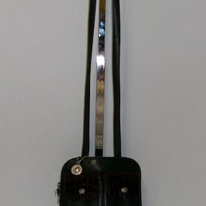 May include: A black leather handbag with a dark brown crocodile-textured front pocket and base. The bag has a long, thin strap with a silver metal accent. A small silver charm hangs from the top of the bag.