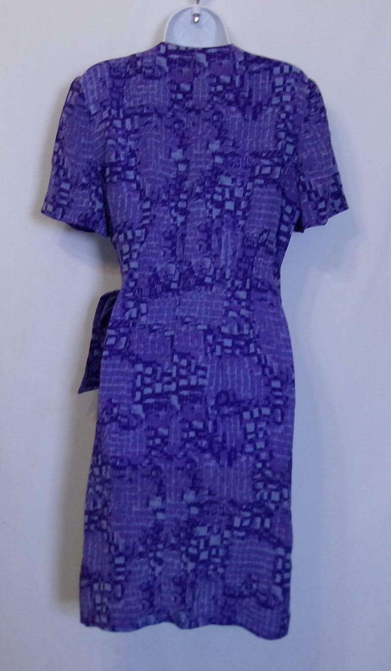 Puede incluir: Un vestido de envoltura de estampado morado y azul con mangas cortas y un lazo en la cintura.
