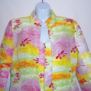 May include: A colorful jacket and top set with a vibrant floral pattern. The jacket features a mandarin collar and a full-length zipper. The fabric has a textured, ribbed appearance with pink, yellow, orange, and green hues. Red floral accents are scattered across the garment.