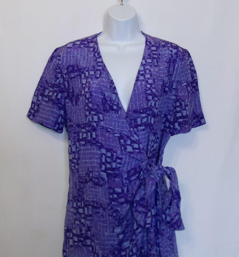 Puede incluir: Un vestido de envoltura de estampado morado y azul con mangas cortas y un lazo en la cintura.