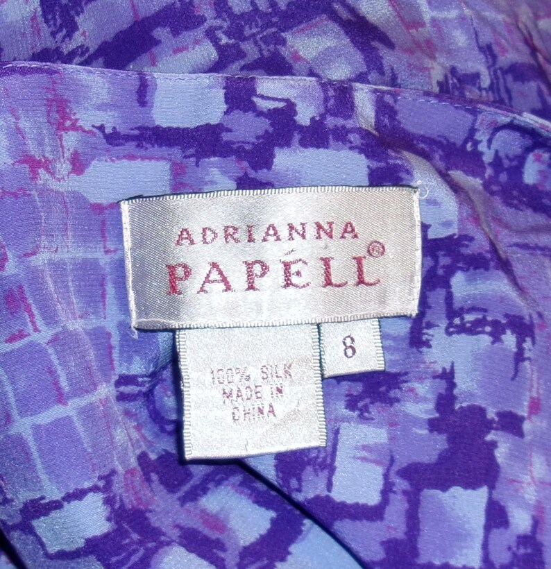 Puede incluir: Una etiqueta blanca con el texto "Adrianna Papell" en letras rojas. La etiqueta tambi&eacute;n tiene una etiqueta de talla 8 y una etiqueta m&aacute;s peque&ntilde;a que dice "100% Seda Hecho en China".