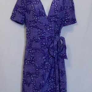 Puede incluir: Un vestido de envoltura de color morado y azul claro con estampado, mangas cortas y un lazo en la cintura.
