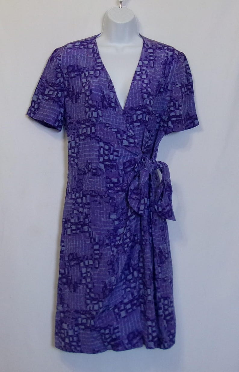 Puede incluir: Un vestido de envoltura de color morado y azul claro con estampado, mangas cortas y un lazo en la cintura.
