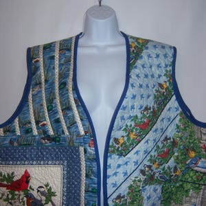 May include: A blue quilted vest with a variety of bird and nature patterns. The vest has a V-neck and is made of a soft, comfortable fabric.