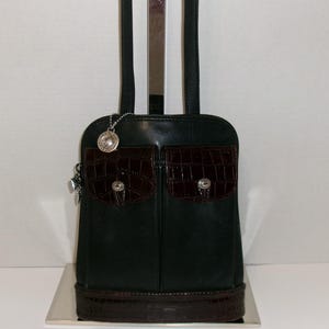 May include: Black leather shoulder bag with two front pockets featuring a dark brown crocodile-textured flap and silver-tone hardware. The bag has a matching crocodile-textured base and a silver charm. The bag has black shoulder straps.