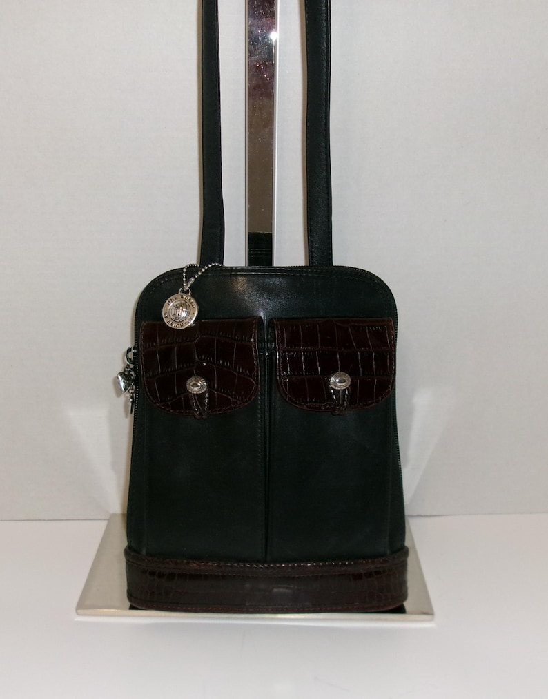 May include: Black leather shoulder bag with two front pockets featuring a dark brown crocodile-textured flap and silver-tone hardware. The bag has a matching crocodile-textured base and a silver charm. The bag has black shoulder straps.