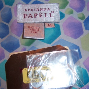 May include: An Adrianna Papell silk garment tag with the number 14, and a tag that reads "Proof of Purchase". The background is a colorful geometric pattern in shades of blue, green, and purple.