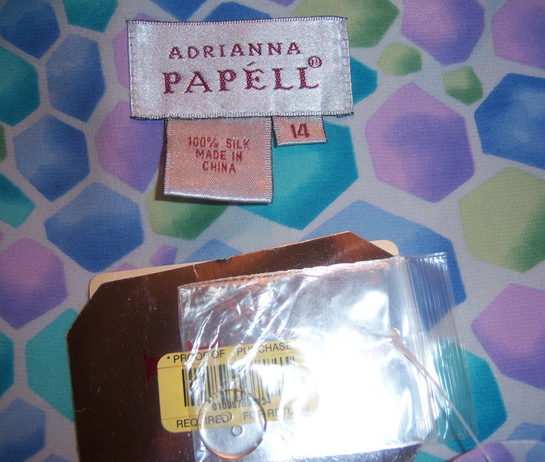 May include: An Adrianna Papell silk garment tag with the number 14, and a tag that reads "Proof of Purchase". The background is a colorful geometric pattern in shades of blue, green, and purple.