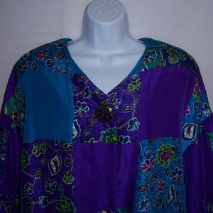 Könnte beinhalten: Eine Patchwork-Bluse mit V-Ausschnitt. Die Bluse ist aus lila und blauem Stoff mit Blumenmustern.