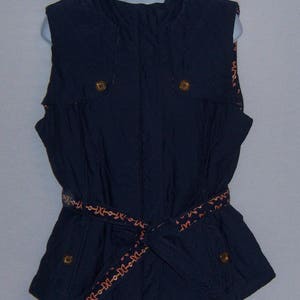 May include: A navy blue sleeveless vest with a zipper closure and a brown belt with a decorative pattern. The vest has two pockets on the front and a high collar.