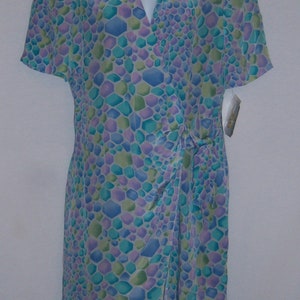 May include: A short-sleeved dress with a V-neck and a wrap-style design. The dress features a pattern of blue, green, and purple geometric shapes. The dress is displayed on a white mannequin.