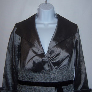 May include: A long-sleeved, silver-grey dress with a wide, black collar and a black velvet belt. The dress has a V-neckline and a sparkly, silver-grey trim around the waist.