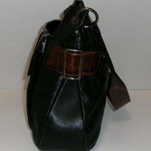 K&ouml;nnte beinhalten: Schwarze Lederhandtasche mit braunem, krokodiltexturiertem Akzentriemen und silberner Schnalle. Die Tasche hat einen Schulterriemen und einen Klappenverschluss. Die Tasche ist dunkelgr&uuml;n.
