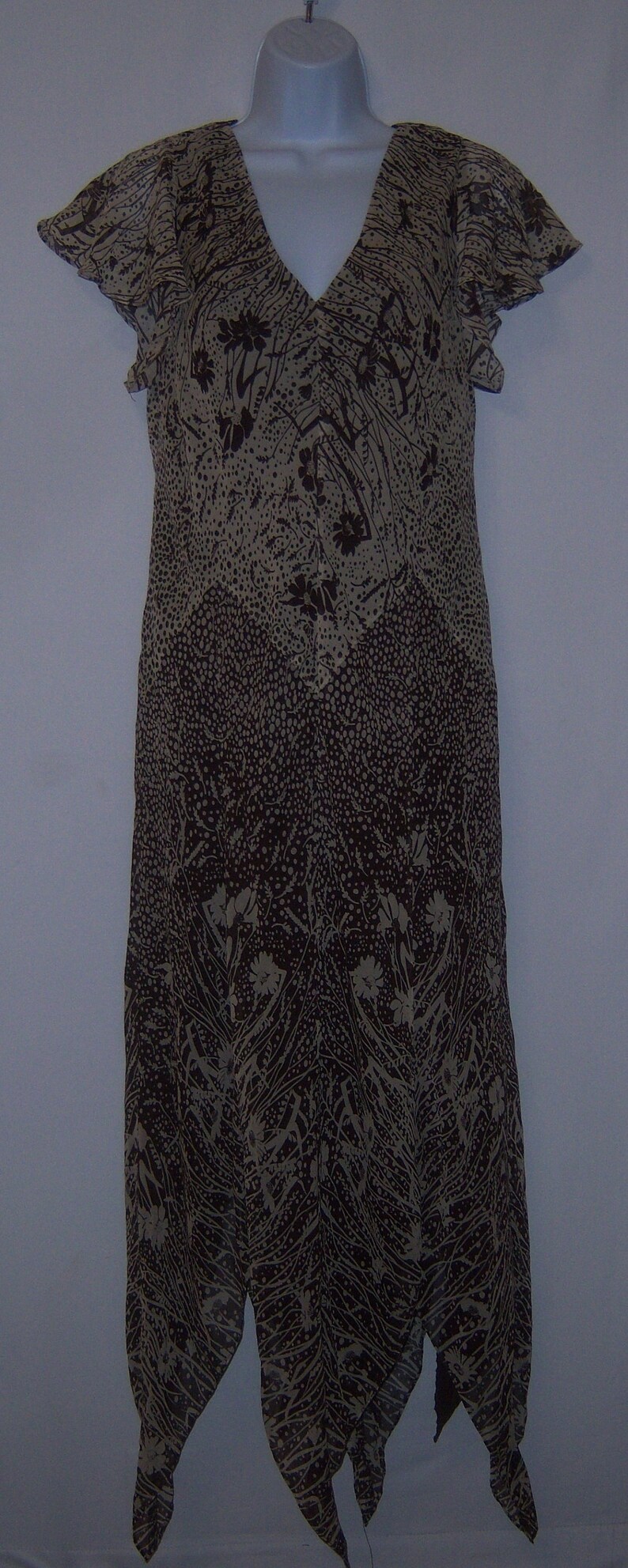 May include: A brown and beige sleeveless dress with a floral print and a V-neckline. The dress has a flowing, asymmetrical hemline.