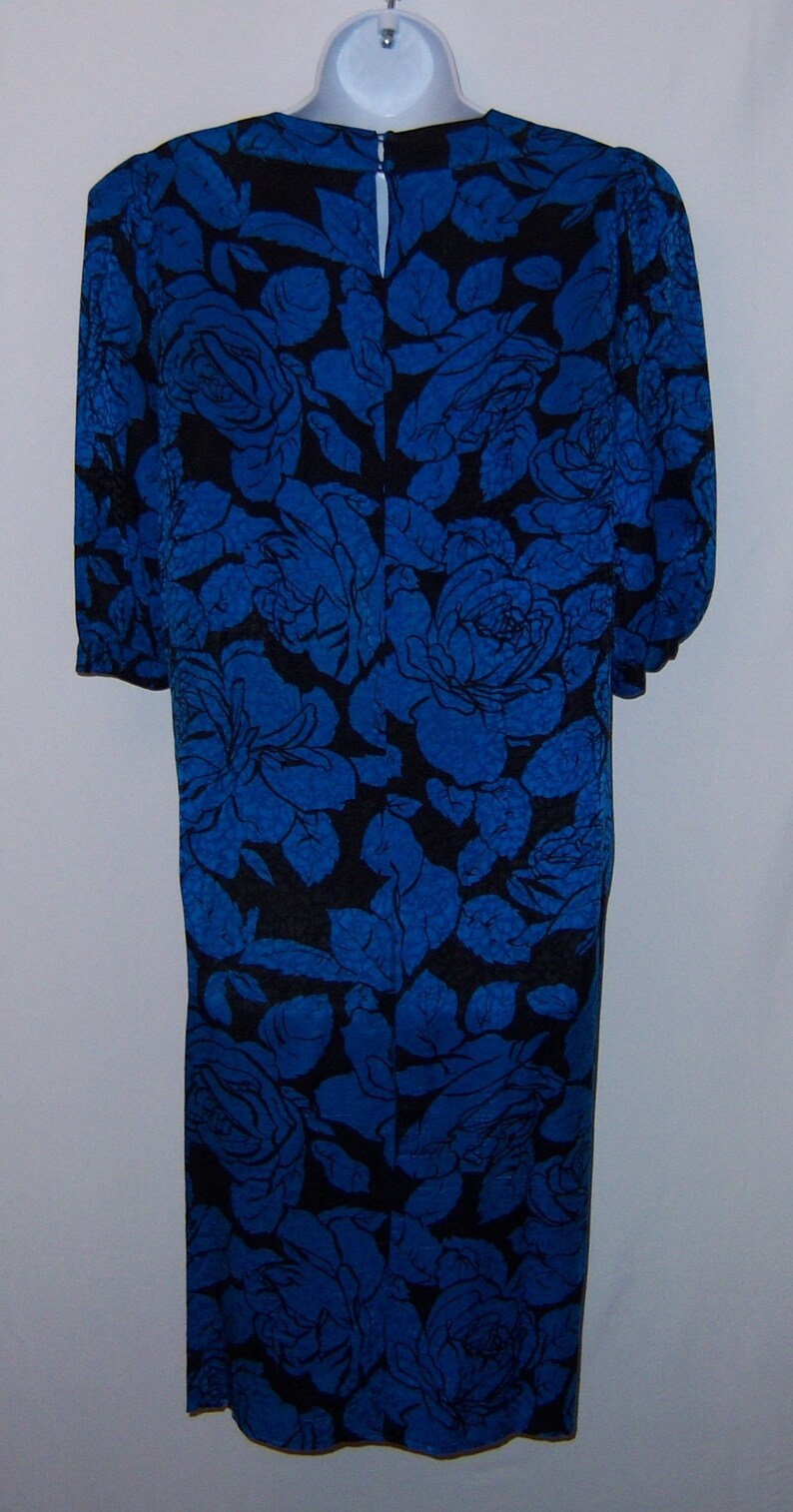 May include: A knee-length dress with a blue floral pattern on a black background. The dress has short sleeves and a keyhole opening at the back of the neck. The floral design features large roses and leaves.