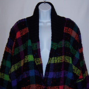 May include: A black and multi-colored plaid cardigan with a black collar. The cardigan is knitted and has a V-neck.