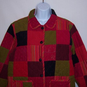 Op de afbeelding: Een rood, groen, zwart en bordeauxrood patchwork gequilte jas met een knoopsluiting.