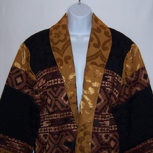 Könnte beinhalten: Eine Jacke mit schwarzem, braunem und goldenem Muster, mit langem, offenem Vorderteil und breitem Kragen. Die Jacke ist aus strukturiertem Stoff und hat ein geometrisches Design.