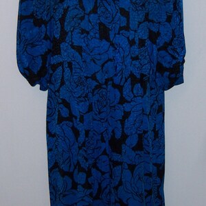 May include: A blue dress with a black floral pattern. The dress has a square neckline and long sleeves. The floral design covers the entire dress, creating a bold and eye-catching look. The dress is displayed on a white mannequin.