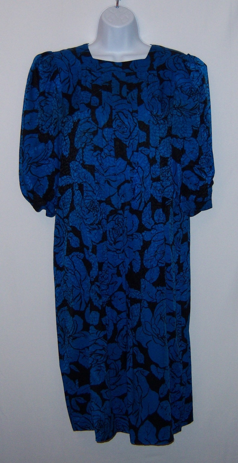 May include: A blue dress with a black floral pattern. The dress has a square neckline and long sleeves. The floral design covers the entire dress, creating a bold and eye-catching look. The dress is displayed on a white mannequin.