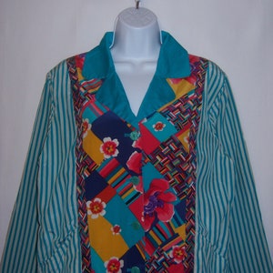 May include: A colorful, long-sleeved shirt with a patchwork design. The shirt features a teal collar and striped sleeves. The patchwork includes floral and geometric patterns in various colors, including red, yellow, and blue.